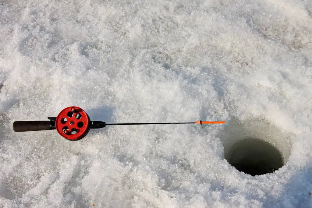 One of the best ice fishing rods lying next to hole in snow