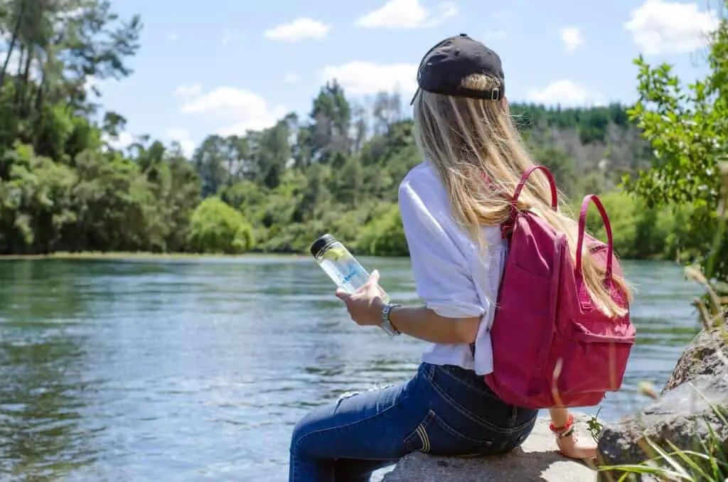 Girl sitting at lake holding reusable water bottle