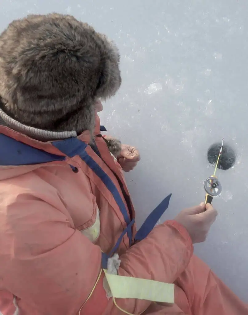 Person ice fishing on a frozen lake holding a rod with one of the best ice fishing reel