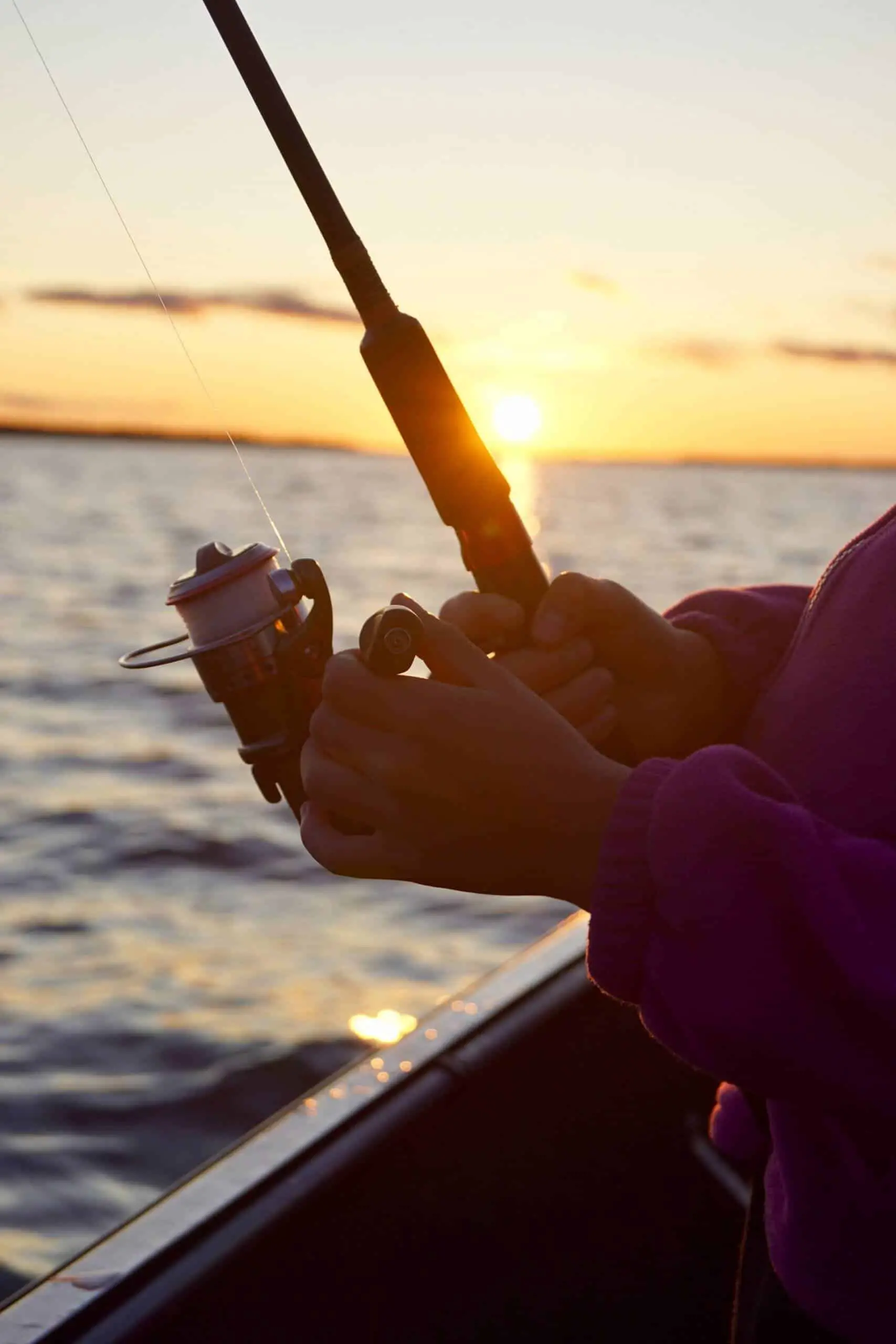Person fishing from a boat with a sunset in the background using one of the best conventional reel for bottom fishing