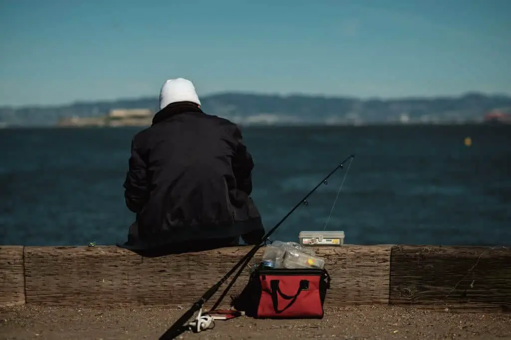Man in black jacket sitting at a dock with a fishing rod and its best line for crappie in the water