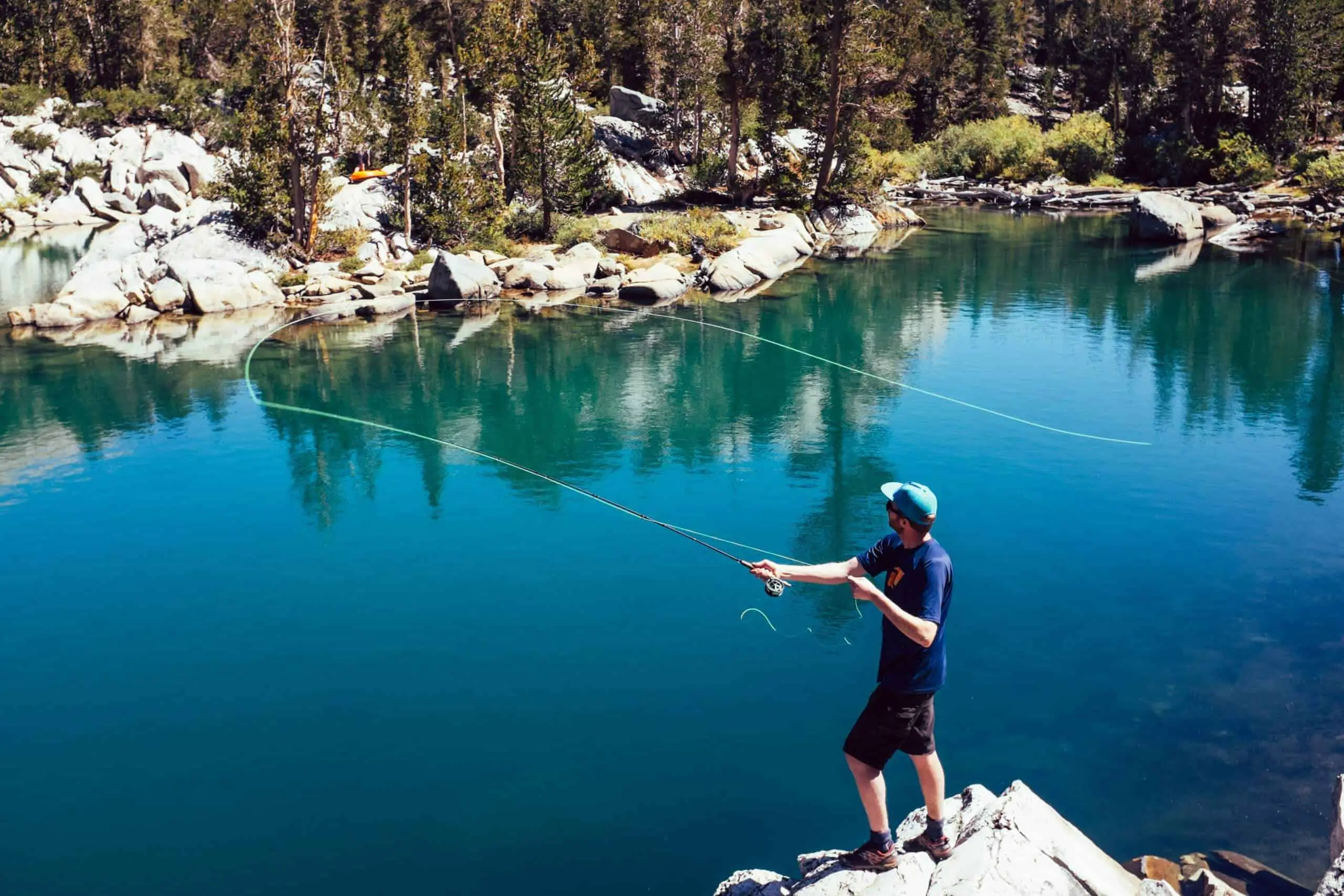 Man standing on rocks fly fishing in a lake