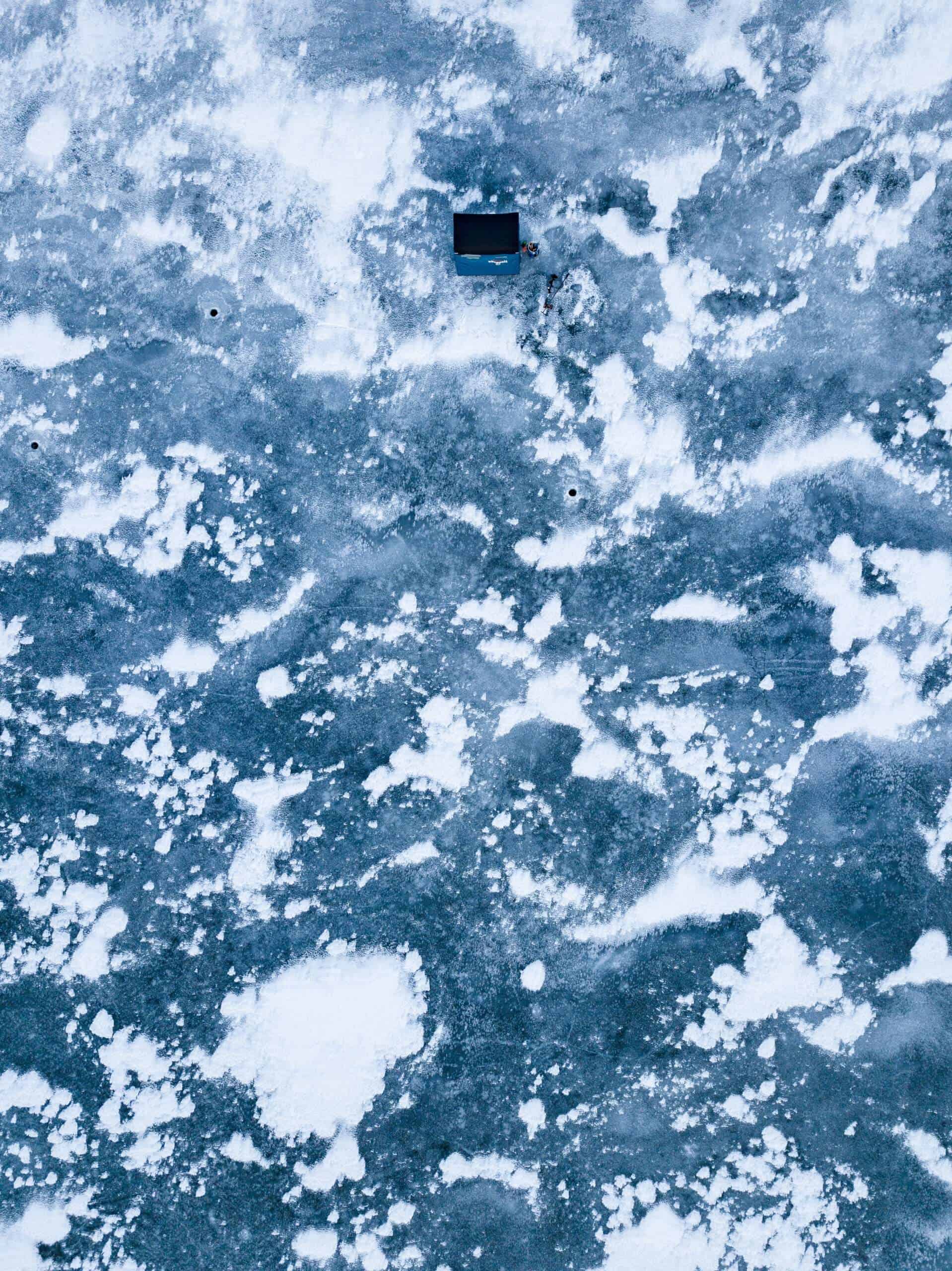 One of the best ice fishing shelter standing on a frozen lake with ice fishing holes in it