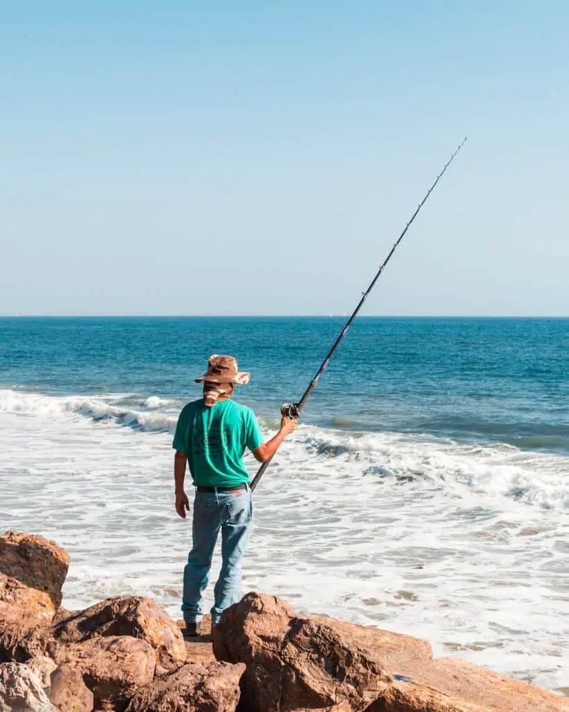 Man standing on rocks holding one of the best baitcasting rod under $100 in the ocean