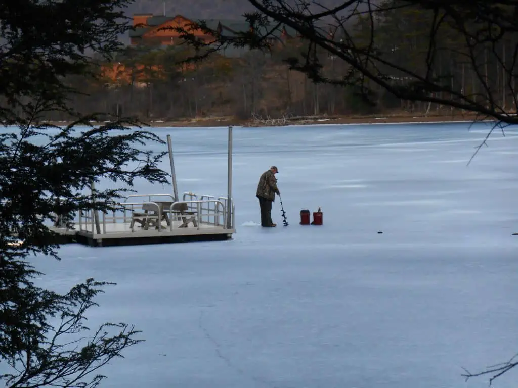 Man standing on a frozen lake using one of the best battery powered ice augers