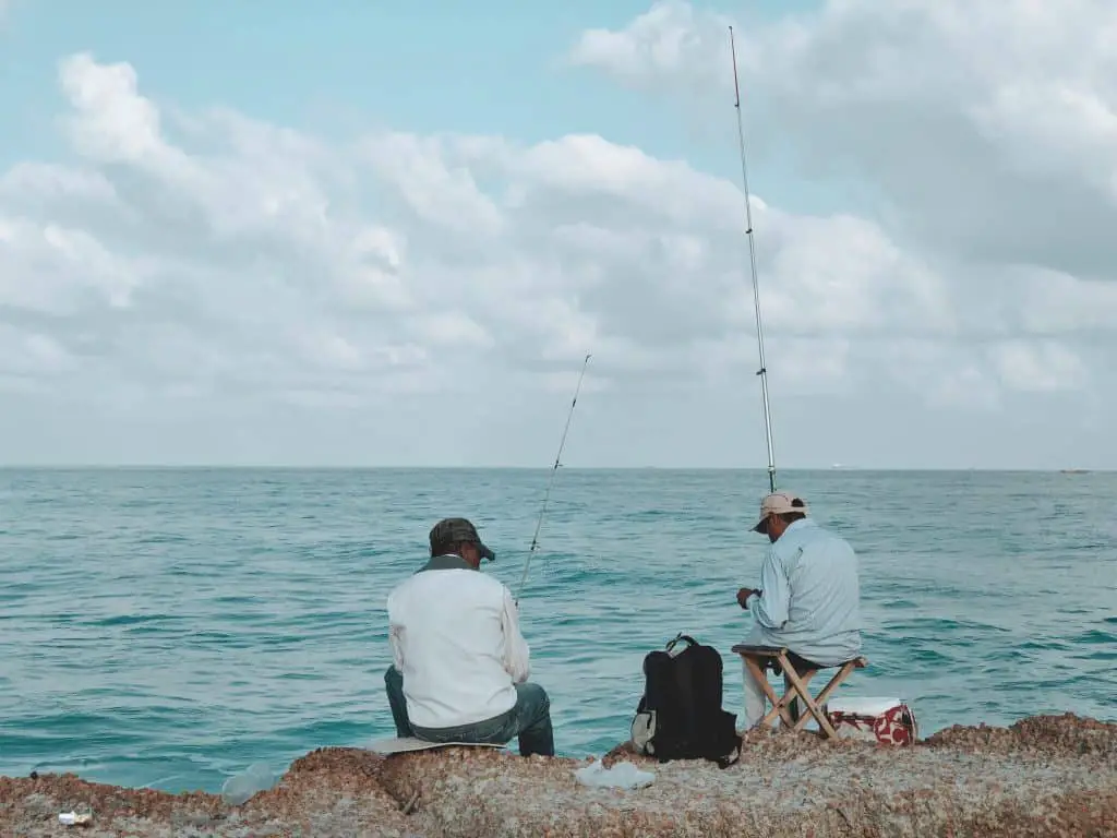 Fishing requires patience: two men sitting on rocks in front of the ocean holding rods waiting for fish to bite