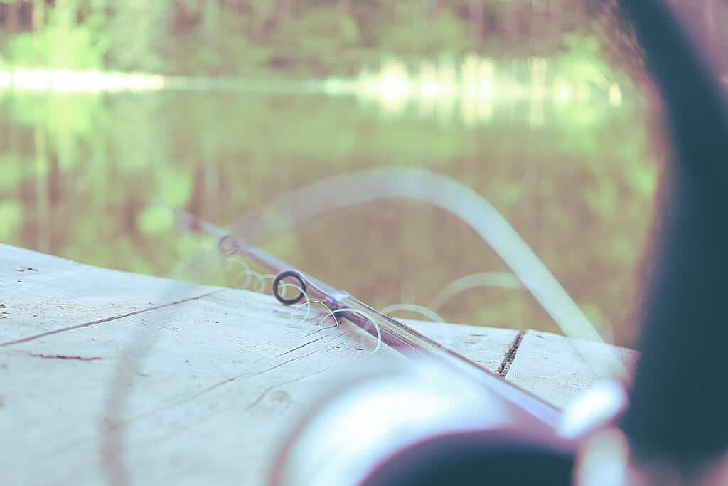 A rod with spiralling fishing line lying on the wooden ground