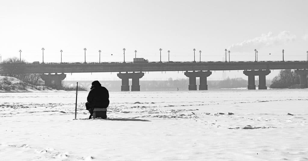 Person sitting in frozen river wearing one of the best ice fishing bibs available
