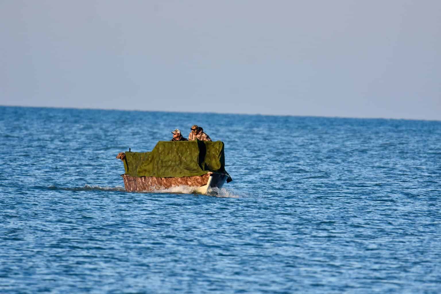 Two men and a dog on a boat going hunting using one of the best bowfishing reels