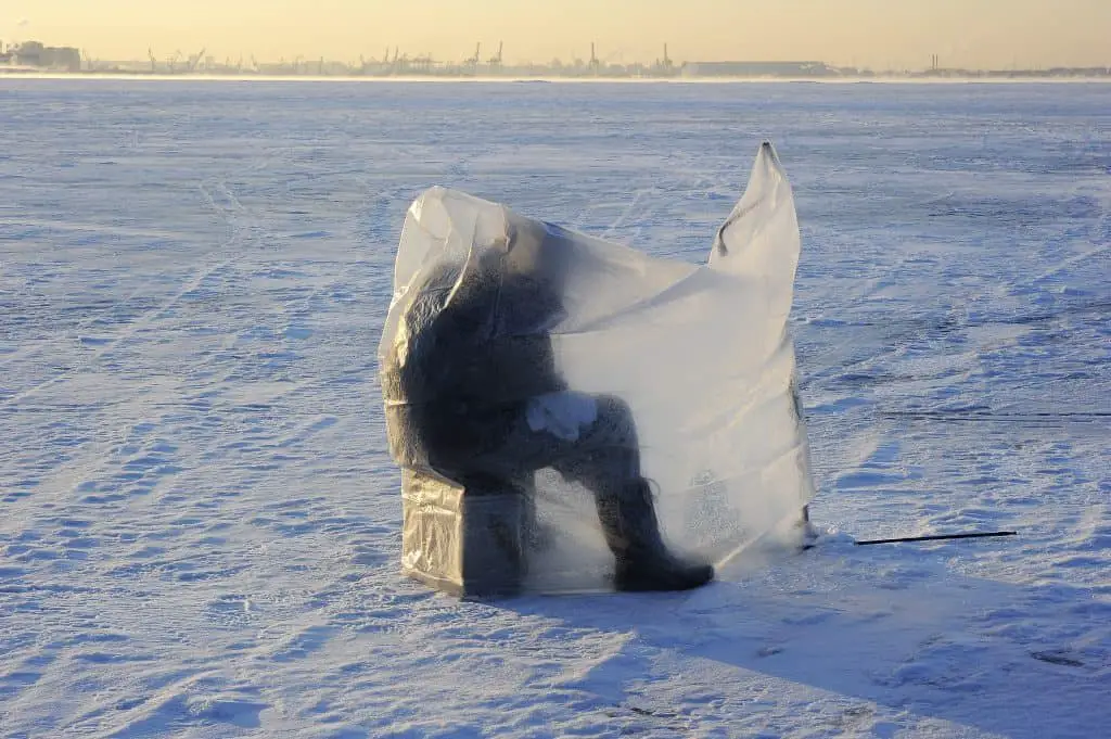 A man practicing sport fishing on the ice sitting covered under plastic