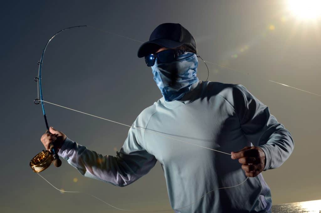 man using one of the best best face shield for fishing with rod and reel casting in morning on ocean