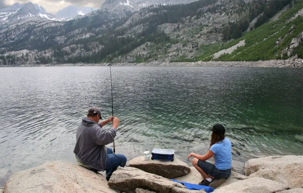 Father and daughter fishing in a High Sierras lake with a waterproof tackle box next to them