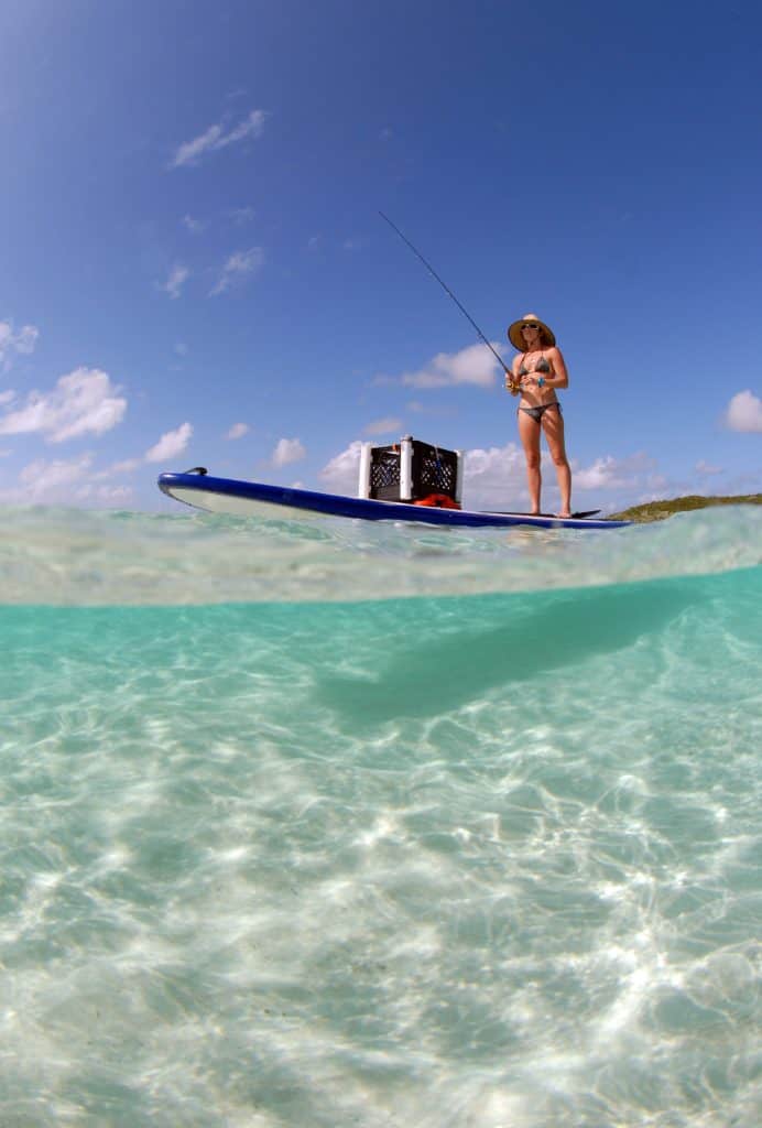 woman in bikini fishing from paddle board in tropical destination