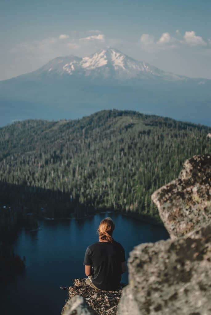 A woman sitting on a mountain overlooking a lake where there is great fly fishing in redding