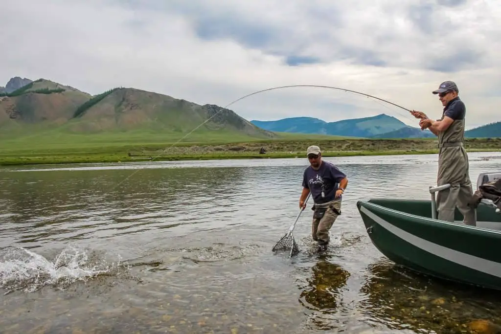 A fly fisherman with a Taimen Trout on the end of his line from a boat, on the Delger Moron river in Mongolia, Moron, Mongolia - July 14th 2014