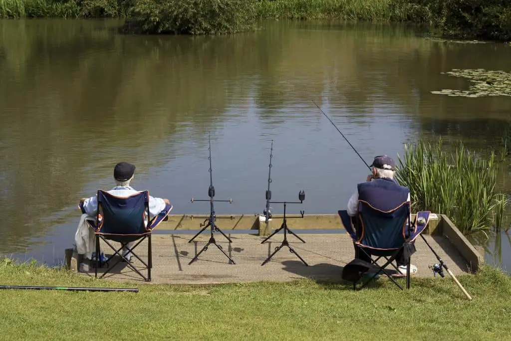 Two elderly men sitting at the edge of a lake fishing.